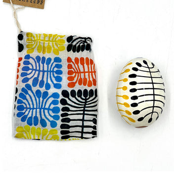 An egg ornament next to a matching fabric bag. Both items are printed with artwork by Mitjili Napurrula.