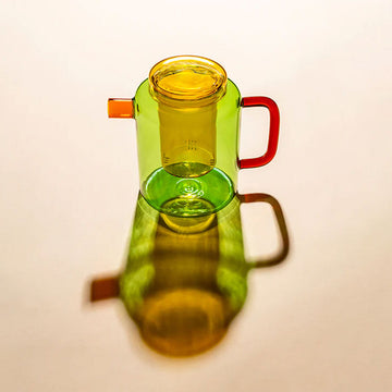 Colorful glass pot with a red handle on a beige background.