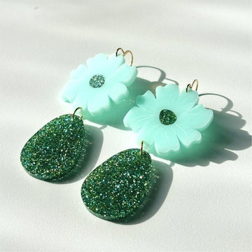 A pair of drop earrings with an aqua coloured flower and green glitter tear drop hanging below.