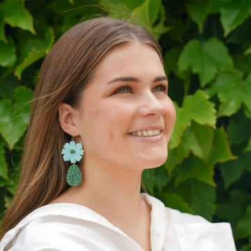 A pair of drop earrings with an lavender coloured flower and white pearl tear drop hanging below.