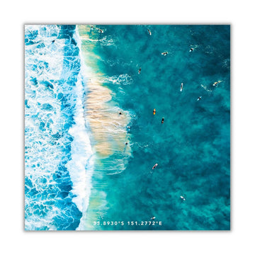 A large beach towel printed with a top down view photo of people swimming at the beach.