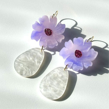 A pair of drop earrings with an lavender coloured flower and white pearl tear drop hanging below.