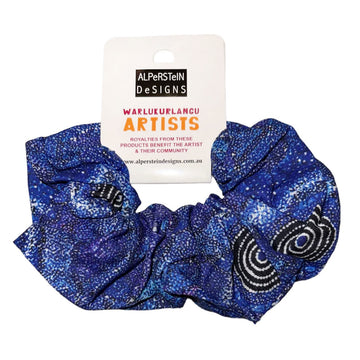 A cotton scrunchie printed with artwork by Alma Nungarrayi Granites in blue and black attached to a white product label.