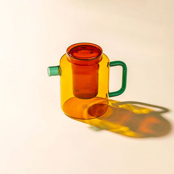 Colorful glass pot with a green handle on a beige background.
