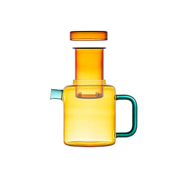 Colorful glass pot with a green handle on a beige background.