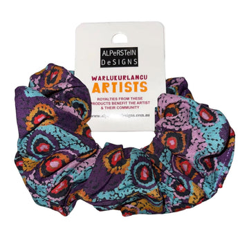 A cotton scrunchie in purple printed with artwork by Magda Nakamarra Curtis in blue, red and pink.