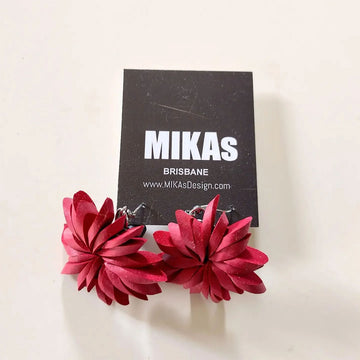 A pair of floral shaped earrings in red attached to hooks.