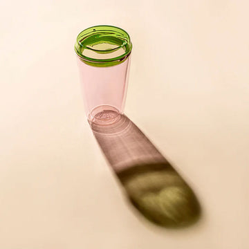 Pink glass with green rim on a beige background.
