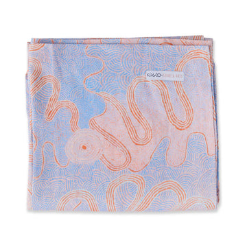 A folded up tablecloth printed with Indigenous artwork in purple and orange.