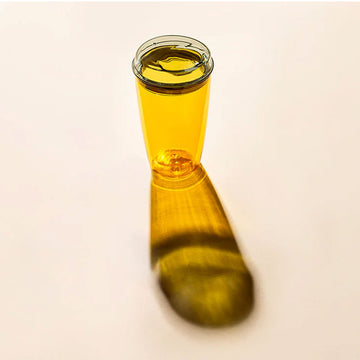 Yellow glass container filled with liquid on a beige background.