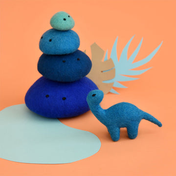 A blue brontosaurus made from felt with a stack of blue felt rocks behind.