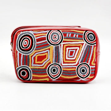 A red leather toiletry bag embroidered with artwork by Mary Napangardi Brown with circles and lines in black, white and yellow.