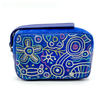 A rectangle velvet toiletry bag in blue embroidered with artwork by Cedric Varcoe with a blue wrist strap on top of the bag.
