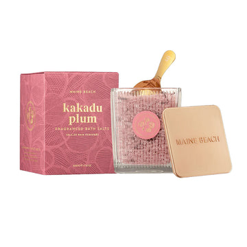 A pink box with the heading 'kakadu plum' written in gold is behind a clear jar filled with pink bath salts with a gold scoop inside.