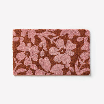 A door mat in red printed with light pink flowers.