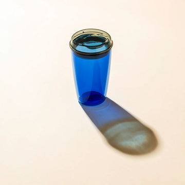 Blue glass tumbler with a black rim on a beige background.
