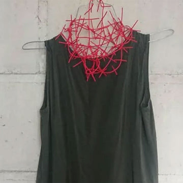 A red necklace made from rubber that looks like a spiderweb over a dark green dress.