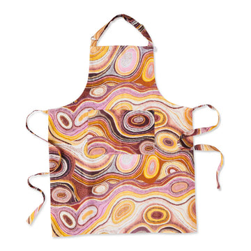 A linen apron is lying flat and printed with Indigenous artwork in shades of brown and pink.