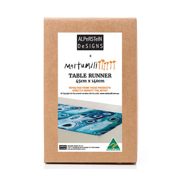 A brown box with a large product label on the front with a photo of the table runner inside printed with artwork by May Wokka Chapman.