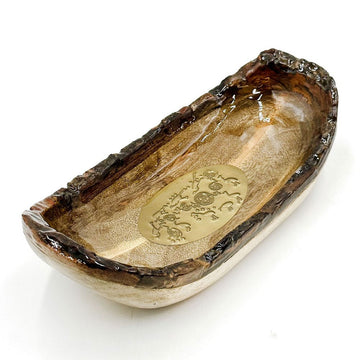 A wooden bowl with rigid edges with an oval gold medallion in the middle with artwork by Cedric Varcoe.