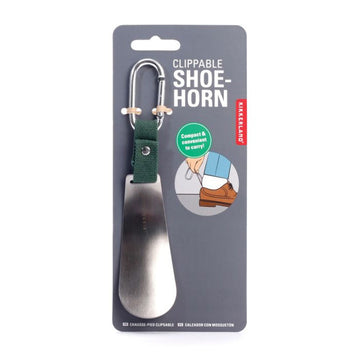 A metal shoehorn attached to a short green strap and silver clip on a grey card.