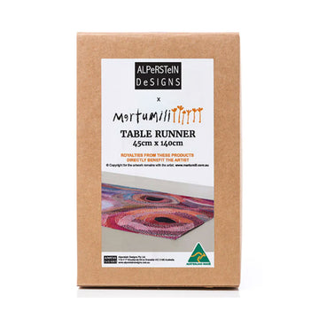 A brown box with a large product label on the front with an image of the table runner inside printed with artwork by Marianne Burton.