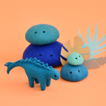 A blue stegosaurus made from felt with two stacks of blue felt rocks behind.