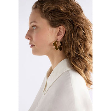 Gold hoop earrings in an abstract shape on a light gray background.