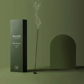 A tall green box next to a burning incense stick with a green background behind.