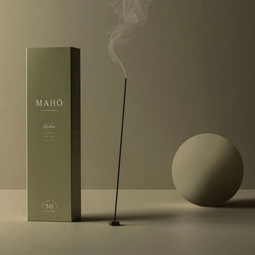 A burning incense stick next to a tall green box against a matching green background.