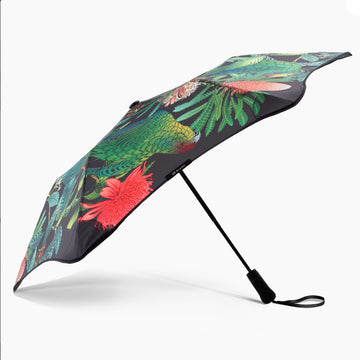 An umbrella standing up and printed with birds and flowers in red and green.