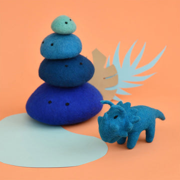 A blue triceratops made from felt with a stack of blue felt rocks behind.