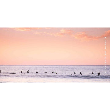 A beach towel printed with a photo of people in the ocean at sunrise.