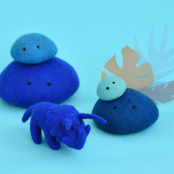 A cobalt blue triceratops made from felt with blue felt rocks surrounding.