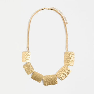 Gold necklace with geometric pendants on a light gray background.