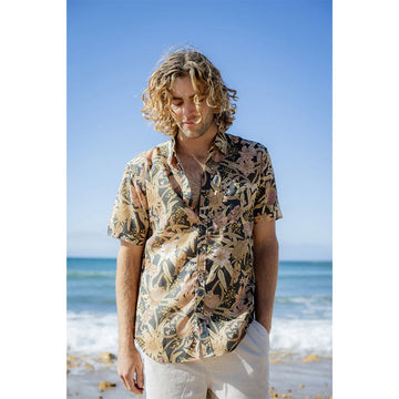 Close up of a man wearing a banksia floral patterned short sleeve shirt while standing at the beach.