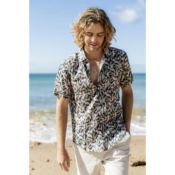 Close up of a man wearing a floral patterned short sleeve shirt while standing at the beach.