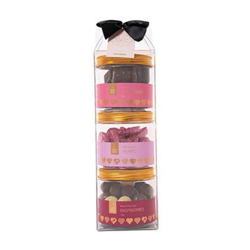 A clear cylinder packaged filled with three round containers of different chocolates. There is a black box on the top.