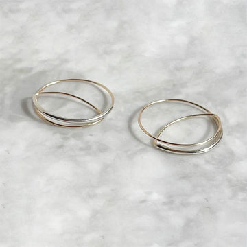 Pair of silver and gold hoop earrings on a light marble background.