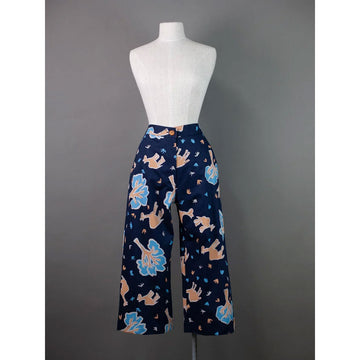 Front view of navy blue pants with colorful patterns of camels and trees on a mannequin against a gray background.