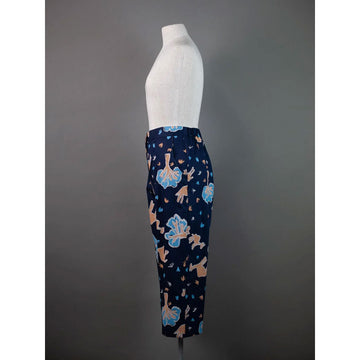 Front view of navy blue pants with colorful patterns of camels and trees on a mannequin against a gray background.