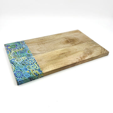 A wooden serving board with a panel on the left of artwork by Cedric Varcoe in blue and yellow.