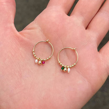Gold hoop earrings with colorful beads on a hand.