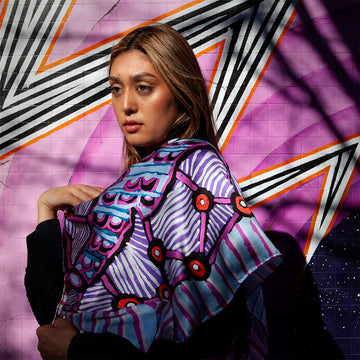 A square silk scarf printed with artwork by Annette Lormada of two fish in purple and yellow.