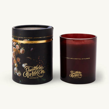 Black candle cylinder packaging with floral design and 'Southern Wild Co' branding next to a red candle with the same branding.