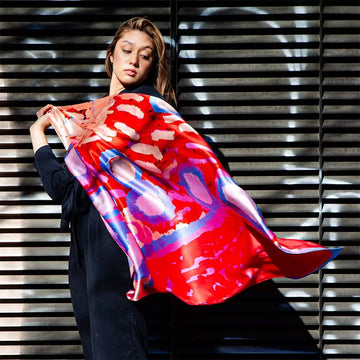 A square silk scarf printed with artwork by Rosie Tarku in red and blue.