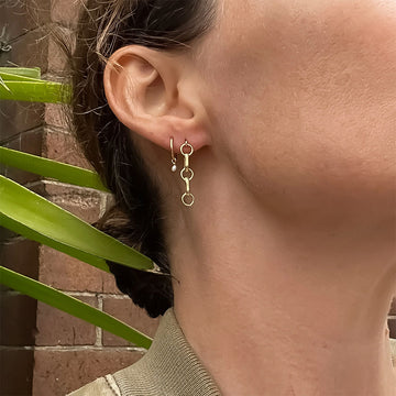 Gold chain earrings on a white stone surface.