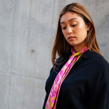 A silk scarf tied up in a knot and printed with artwork by Rosie Tarku in pink.