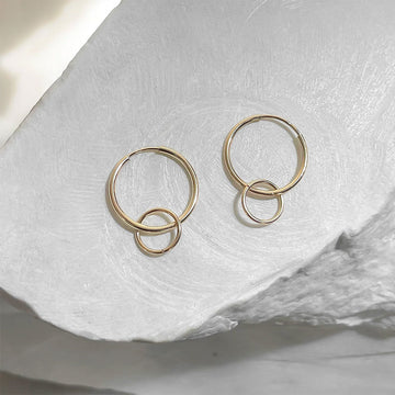Gold hoop earrings on a textured white surface.