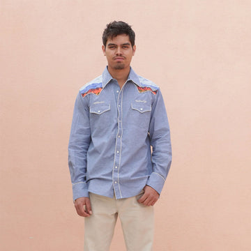 Man wearing a blue denim shirt with Indigenous designs on the shoulders on a beige background.